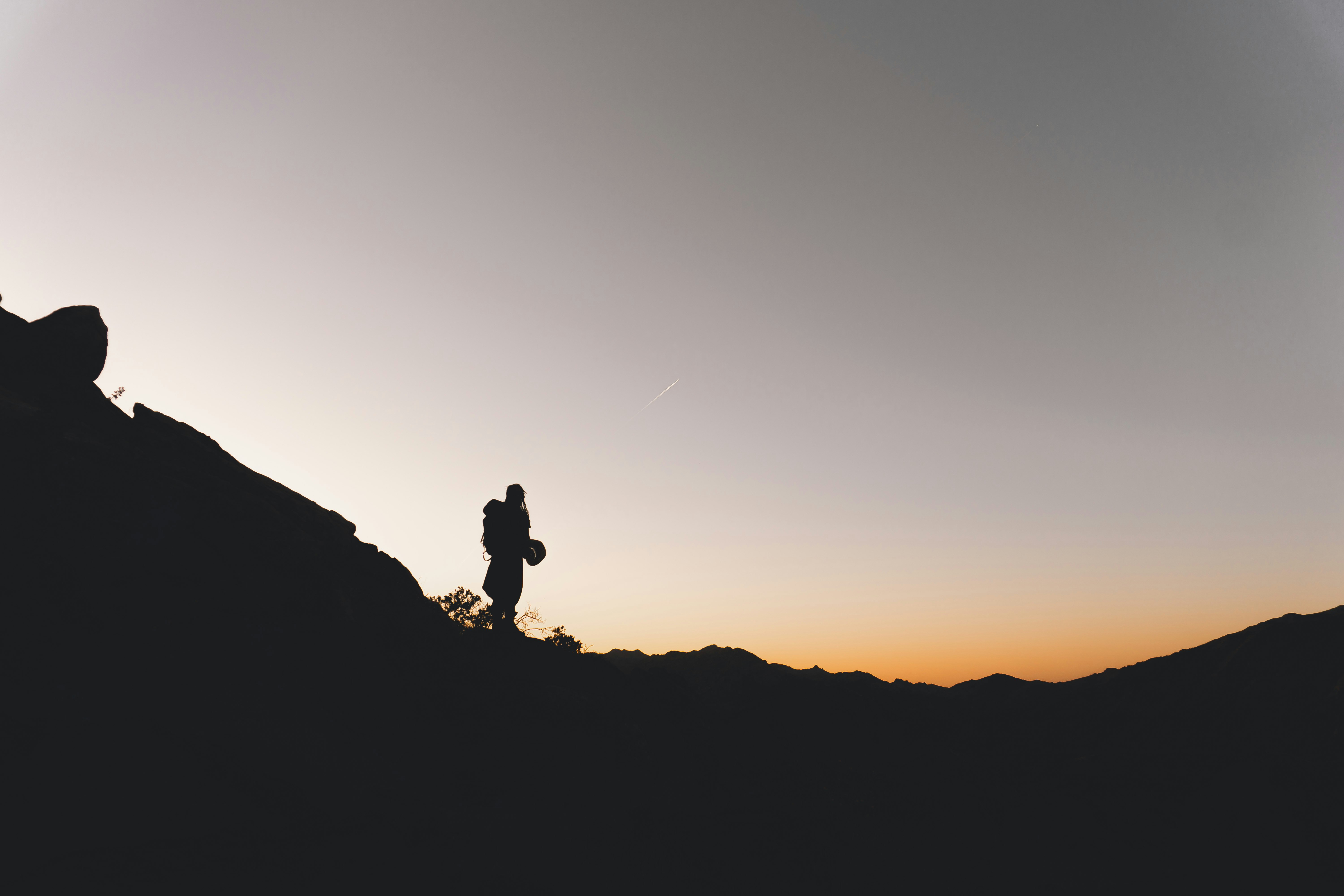 silhouette of man standing on rock formation during sunset